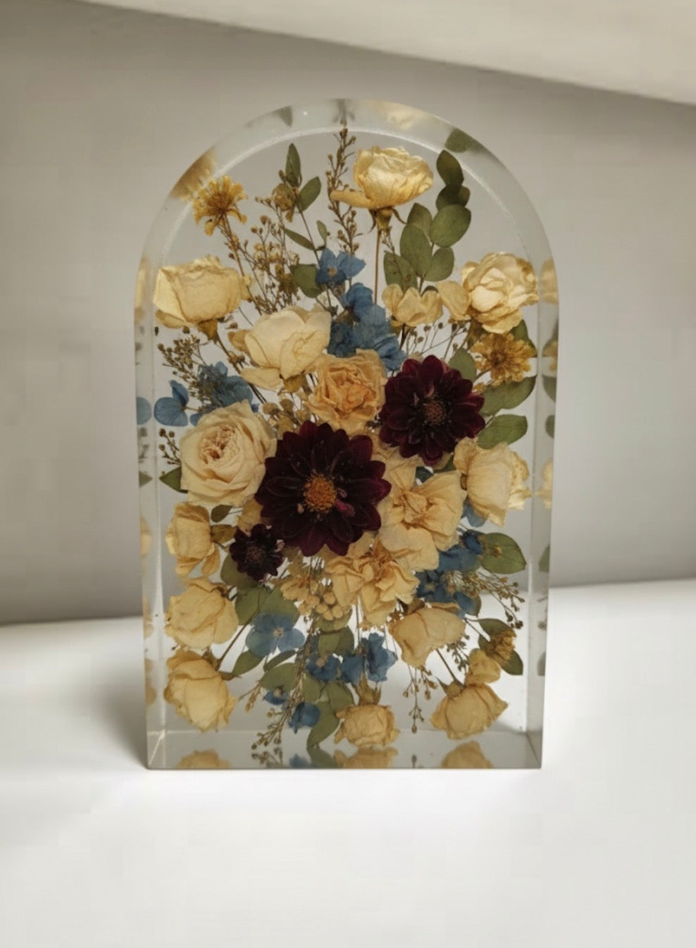 Arch-shaped clear resin display with pressed flowers on a neutral background