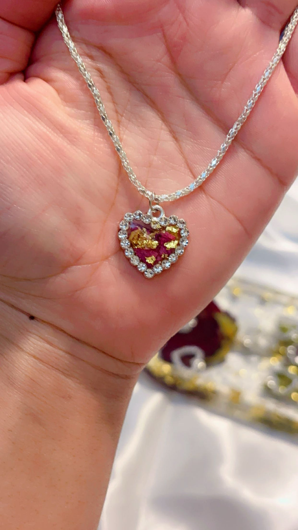 Heart-shaped pendant necklace held in a hand with blurred background made from real rose petals and UV resin 
