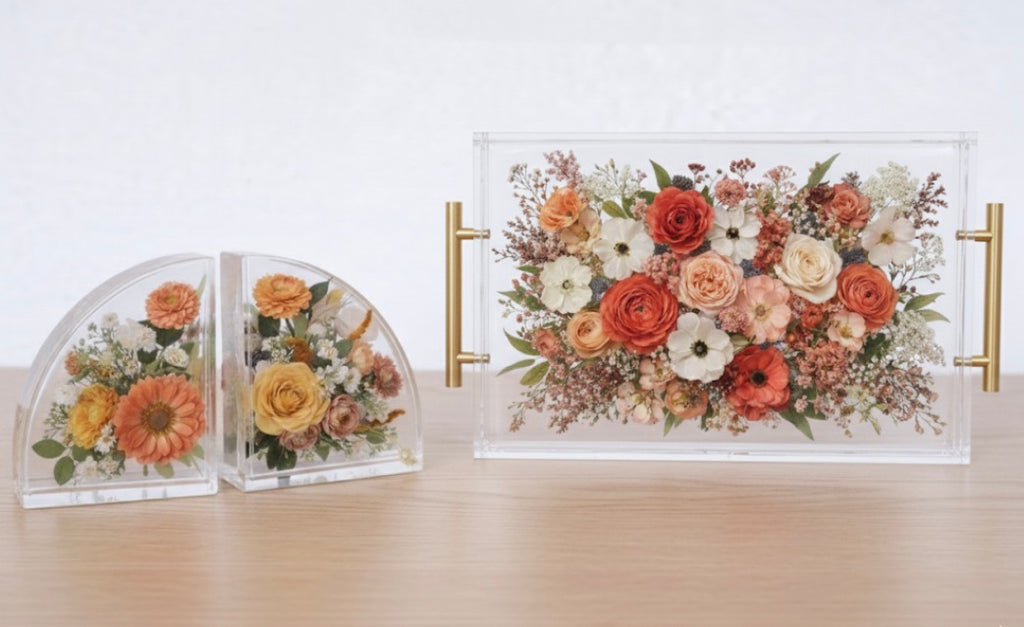 A Set of bookends with preserved flower inside resin and an acrylic display tray with (preserved wedding bouquet) gold handles on a wooden surface.